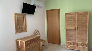 A room with a wooden wardrobe, a small chair, a wall-mounted TV, and a door. - Hotel Ristorante Il Triangolo (Augusta)