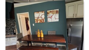 A kitchen with a wooden table, bench, and two yellow salt shakers. There are two abstract paintings on the wall and a stainless steel refrigerator. - A modern country place (Snellville)