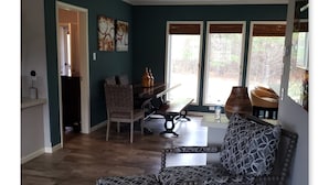 A living room with a dark teal wall, a wooden dining table with chairs, a patterned sofa, and a large window with blinds. - A modern country place (Snellville)