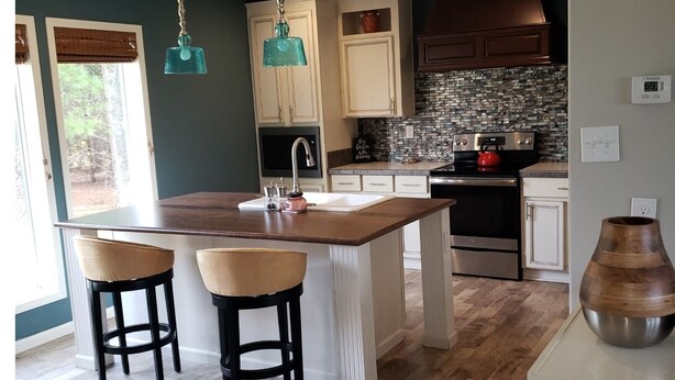 A modern kitchen with a central island, two bar stools, a built-in oven, and a stone backsplash. - A modern country place (Snellville)