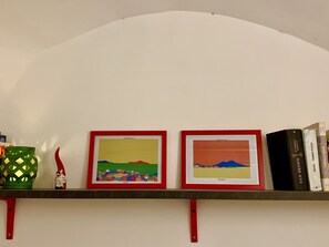 A shelf with two framed artworks, a small figurine, and a few books.