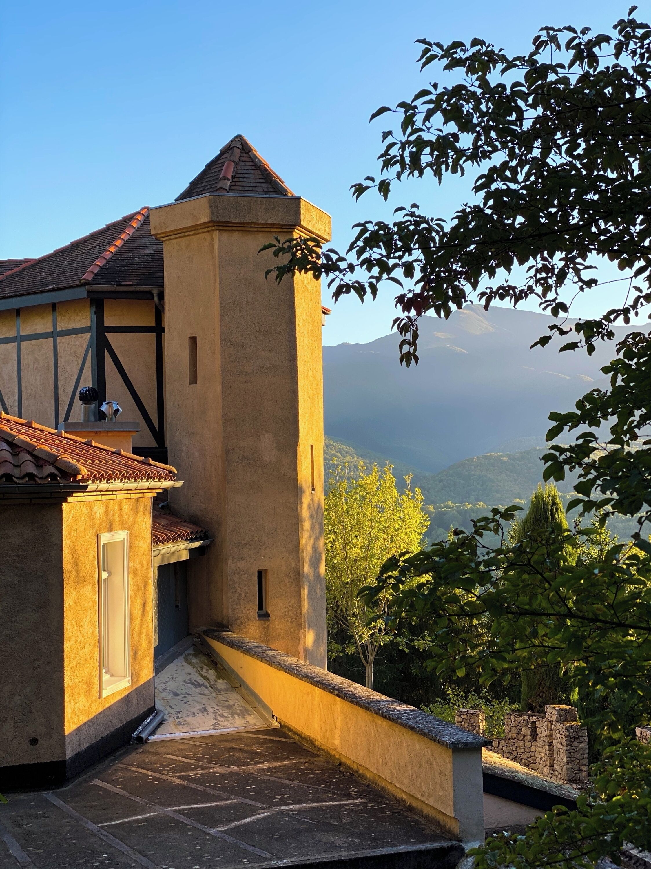 A building with a stone facade, a tiled roof, and a view of a mountainous landscape.