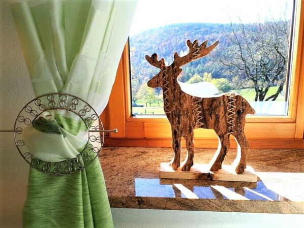 Une fenêtre donnant sur une forêt et une sculpture de cerf en bois, posée sur un socle.