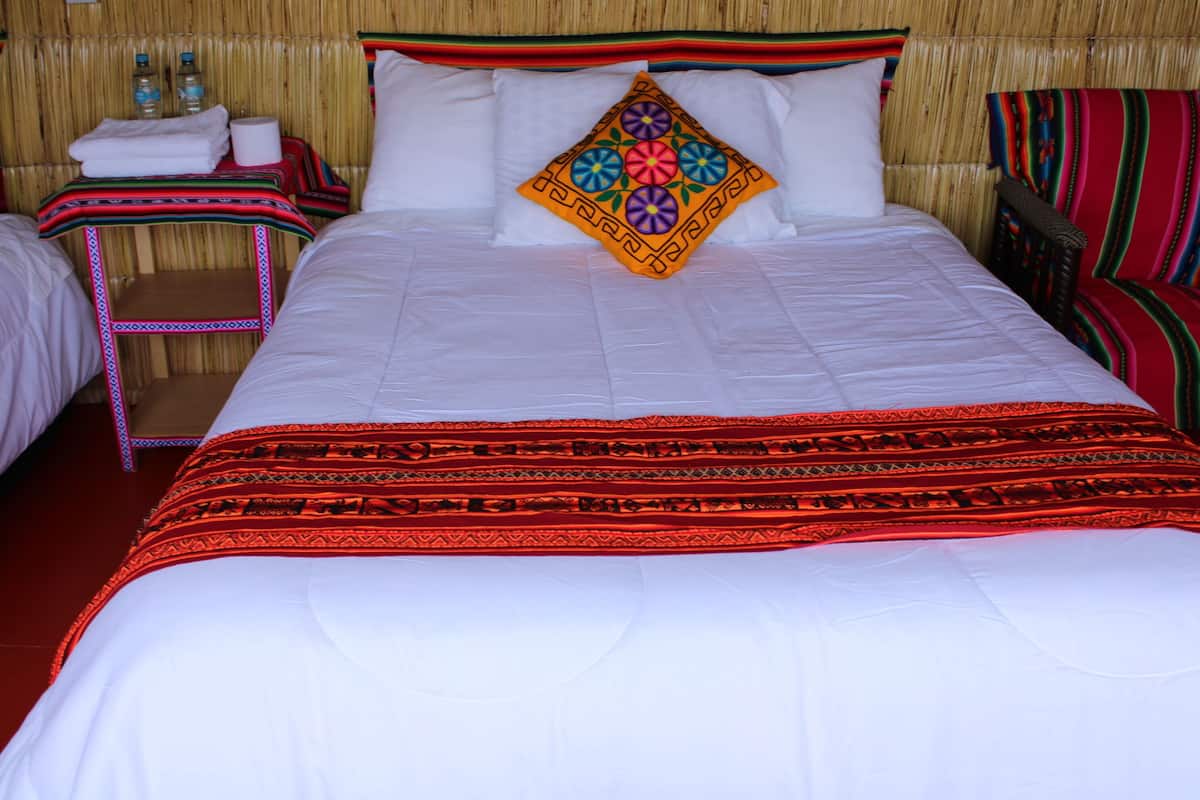 Un lit avec une literie blanche et un coussin coloré, une petite table avec des articles de toilette et une chaise avec un coussin à rayures.