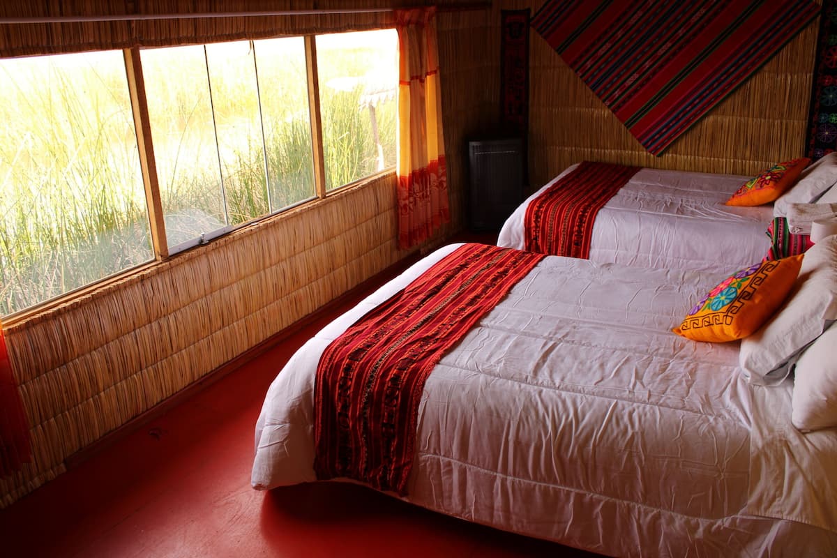 Une chambre avec deux lits, une fenêtre donnant sur un champ d’herbes hautes et un mur décoré d’un motif traditionnel tissé.