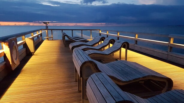 Een houten terras met lounge stoelen en een reling met uitzicht op het water.