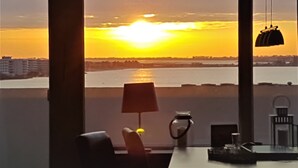 Een kamer met uitzicht op een zonsondergang boven het water, een tafel met een lamp en een stoel.