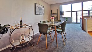 A modern dining area with a glass table, metal chair, and a decorative metal stand with a picture frame.