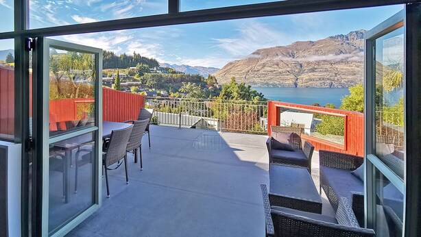 A balcony with a view of a lake and mountains, furnished with wicker chairs and tables.