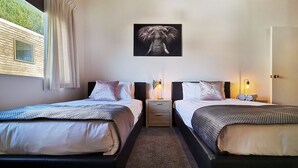 A double room with two beds, a nightstand, a wall-mounted elephant picture, and a window with curtains.