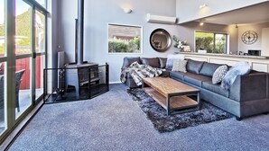A modern living room with a large window, a fireplace, a sofa, a coffee table, and a kitchen area.