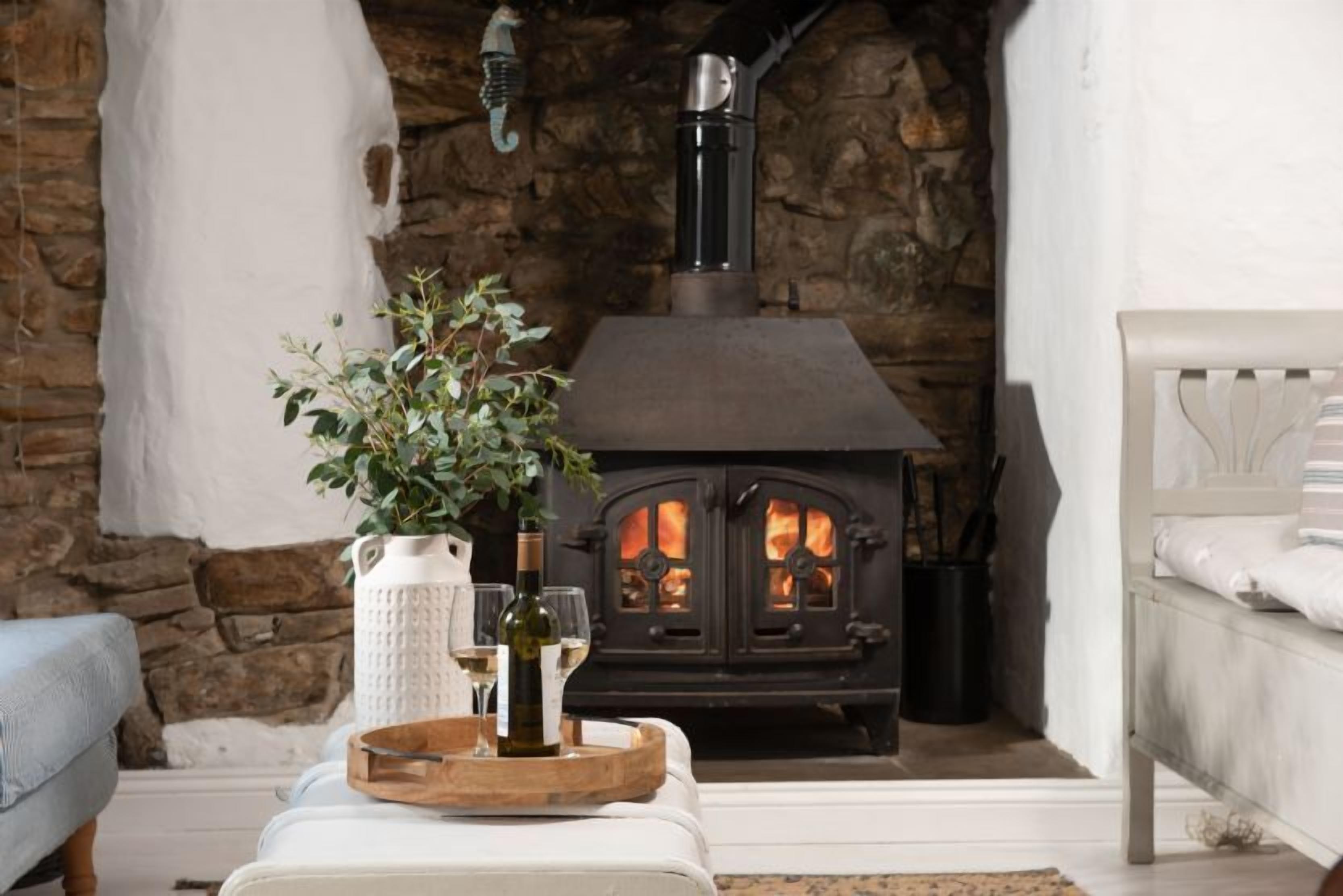A cozy room with a stone wall, a fireplace, a white sofa, and a wooden tray with wine glasses and a bottle.