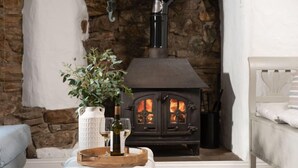 Une pièce chaleureuse avec un mur en pierre, une cheminée, un canapé blanc et un plateau en bois sur lequel sont posés des verres à vin et une bouteille.