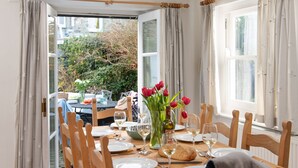 Une table à manger dressée pour six personnes, avec des chaises, un vase de tulipes rouges et une bouteille de vin blanc.