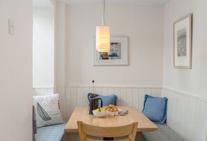 A dining area with a wooden table, blue cushions, a bowl of fruit, and a coffee pot.