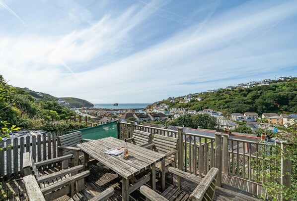 A wooden deck with a table and chairs overlooking a coastal town.