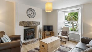 Una sala de estar con chimenea de piedra, un televisor sobre un soporte de madera, un reloj en la pared y una ventana con persianas.