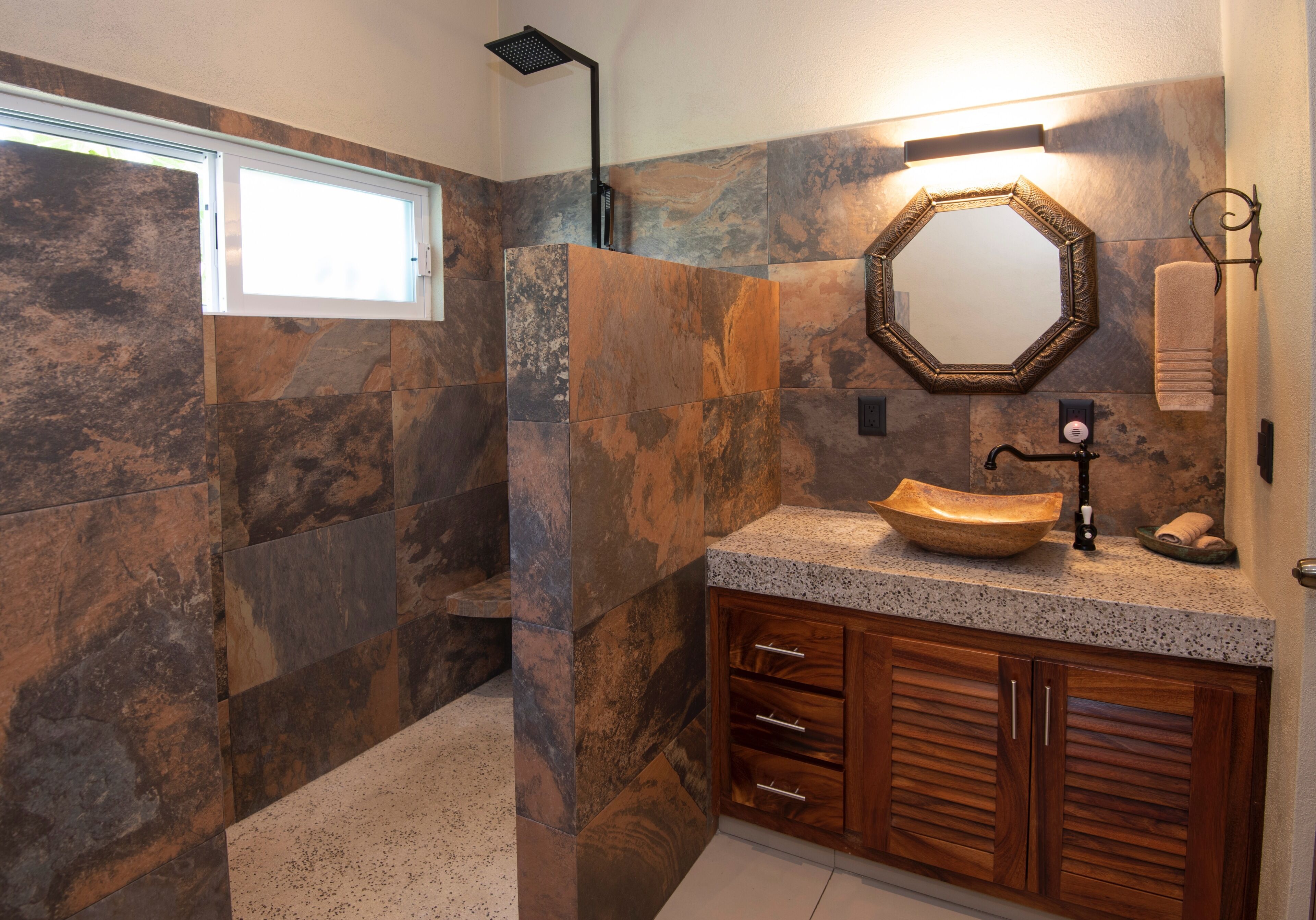 Une salle de bain avec un mur en pierre, un meuble-lavabo en bois, un lavabo avec un bac en forme de coupe, un miroir et un porte-serviettes.