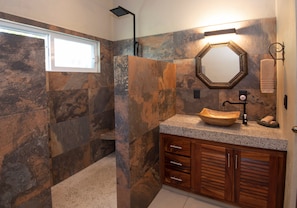 Une salle de bain avec un mur en pierre, un meuble-lavabo en bois, un lavabo avec un bac en forme de coupe, un miroir et un porte-serviettes.