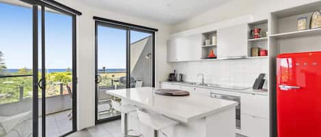 A modern kitchen with a large island, white cabinetry, and a red refrigerator.