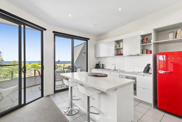 A modern kitchen with a large island, white cabinetry, and a red refrigerator.