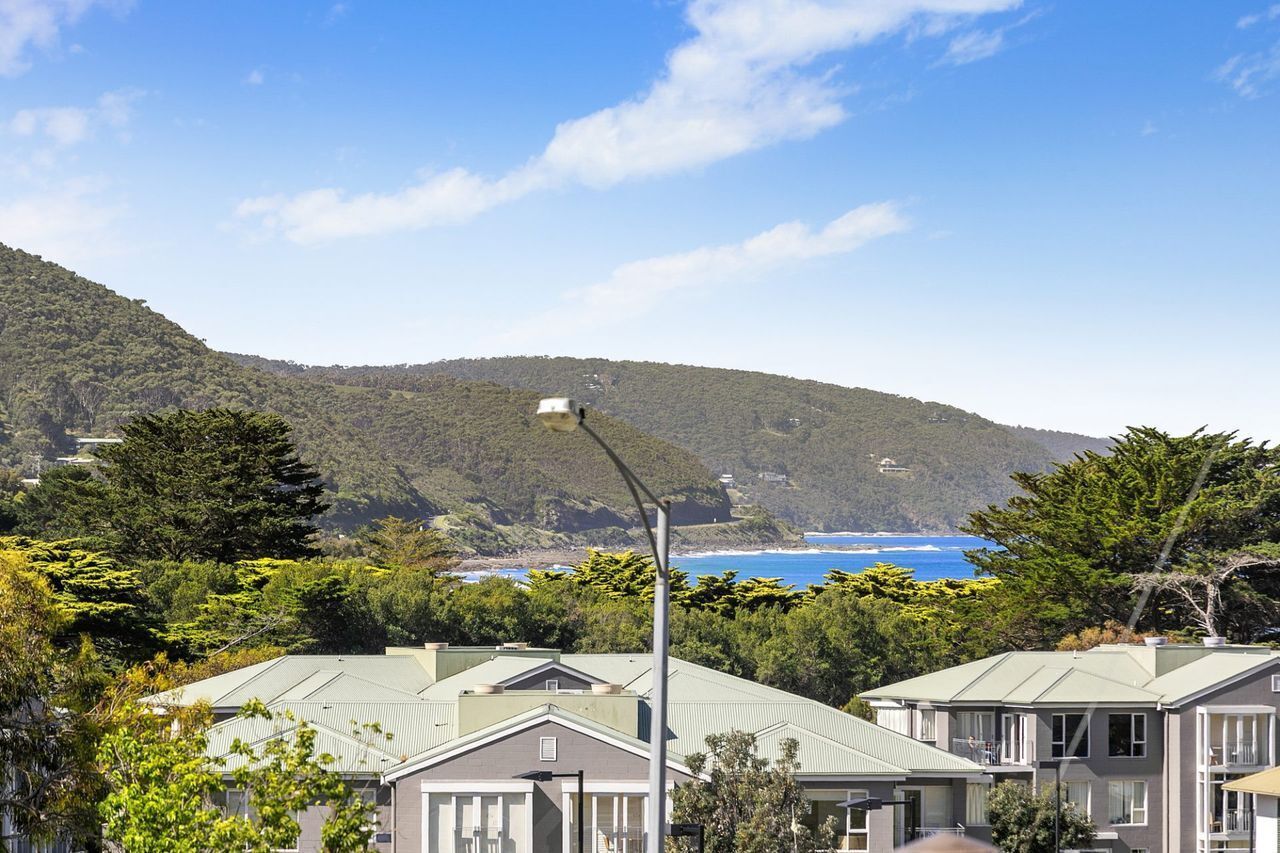A residential area with houses, a street lamp, and a view of a coastline with hills in the background.
