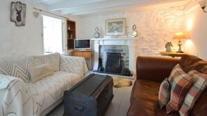 A cozy living room with a fireplace, a sofa, a brown leather couch, and a television. - A spacious, detached cottage with character and charm, located in St Agnes. (St Agnes)