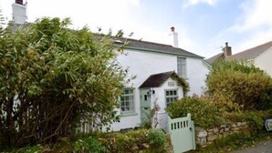 A white building with a green door and windows, surrounded by greenery and a stone wall. - A spacious, detached cottage with character and charm, located in St Agnes. (St Agnes)