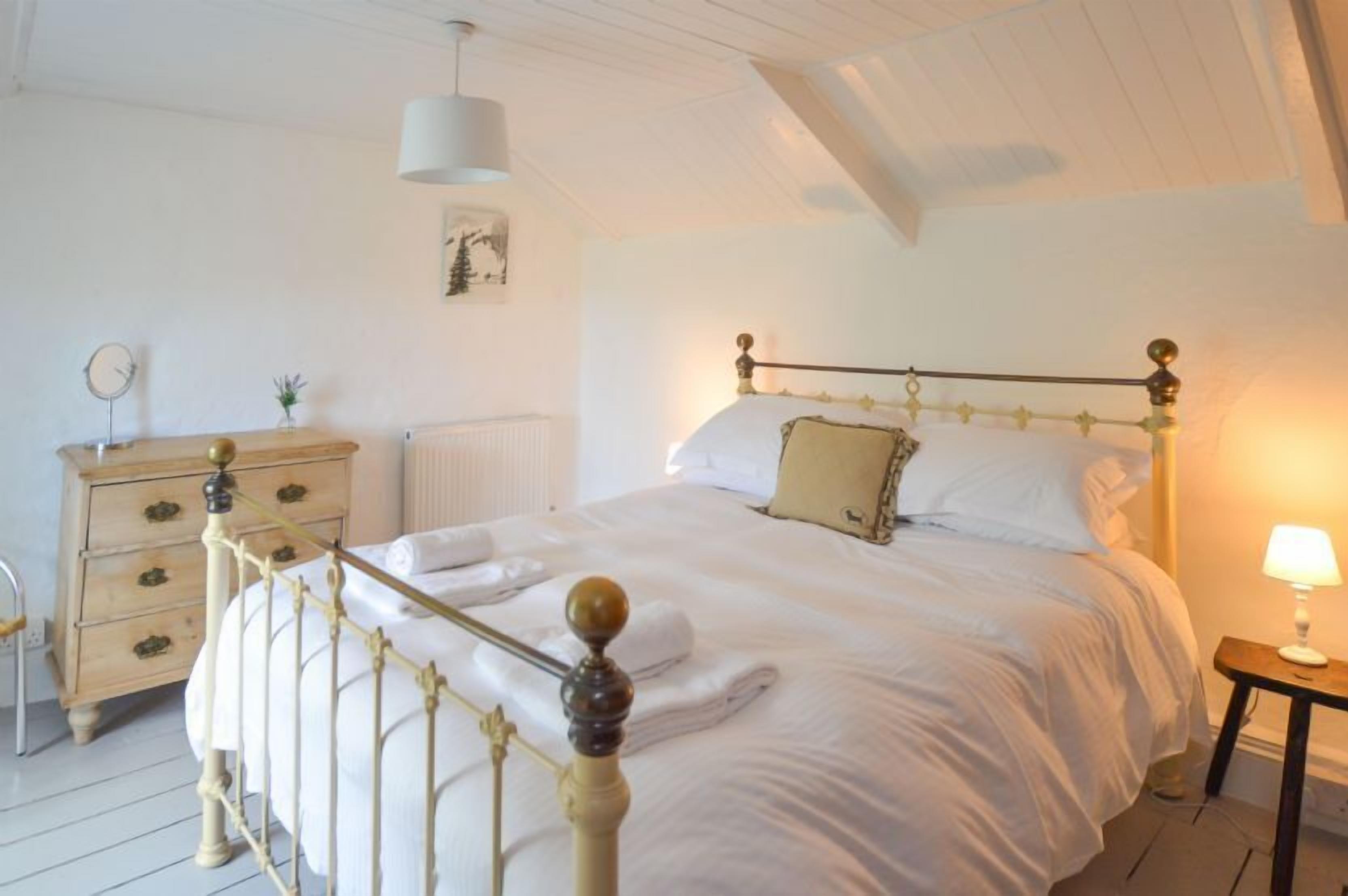 A bedroom with a bed, a dresser, a lamp, and a painting on the wall.