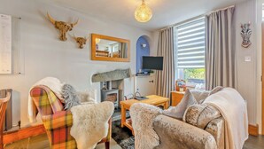 A cozy living room with a fireplace, a television, and a large window with curtains. - 2 bedroom accommodation in Windermere (Windermere)