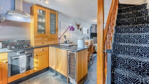 A modern kitchen with wooden cabinets, a gas stove, and a dining area with a patterned rug. - 2 bedroom accommodation in Windermere (Windermere)