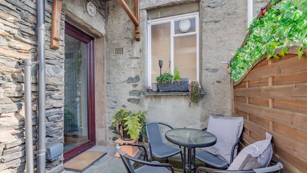 A stone building with a wooden door, a window with a clock, and a small table with chairs. - 2 bedroom accommodation in Windermere (Windermere)