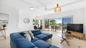 A modern living room with a blue sofa, a TV, and a dining area with a view to the outdoors. - Taralla 8 Noosa Heads (Noosa Heads)