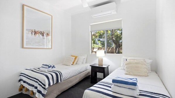A bedroom with two beds, a bedside table, a framed picture, and a window with a view of trees. - Taralla 8 Noosa Heads (Noosa Heads)