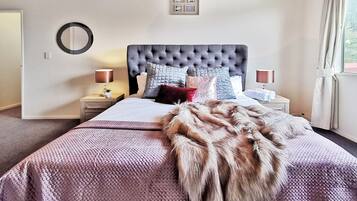 A bedroom with a tufted headboard, a large bed with a patterned bedspread, multiple pillows, bedside tables with lamps, and a framed picture on the wall.