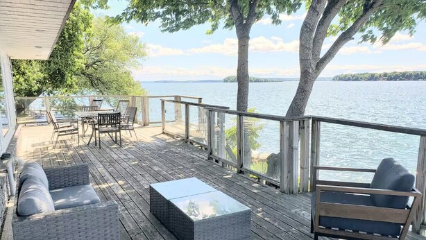 A wooden deck with outdoor furniture, including sofas and a coffee table, overlooking a body of water. - Four Season Waterfront Cottage Over-the-Water view (Orillia)