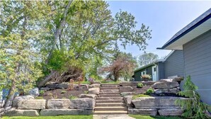 A stone staircase leading to a house with a well-maintained lawn and trees. - Four Season Waterfront Cottage Over-the-Water view (Orillia)