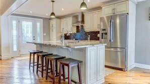 A kitchen with a central island, bar stools, stainless steel appliances, and white cabinetry. - Four Season Waterfront Cottage Over-the-Water view (Orillia)