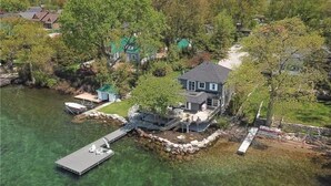 An aerial view of a lakeside property with a dock, a house, and surrounding greenery. - Four Season Waterfront Cottage Over-the-Water view (Orillia)