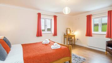 A bedroom with a wooden bed, a desk with a mirror, and two windows with red curtains.