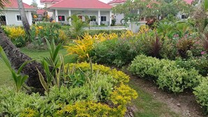 Un jardin bien entretenu, avec différentes espèces de plantes, et un bâtiment avec un toit rouge en arrière-plan.