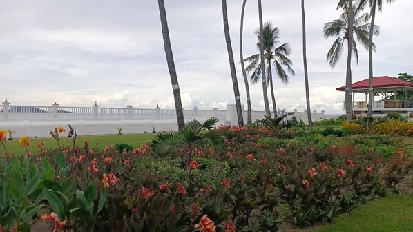 Un jardín ajardinado con palmeras, una cerca blanca y un pabellón de techo rojo.