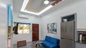 Un espace de vie compact comprenant un coin cuisine, un canapé bleu, une table à manger et un ventilateur de plafond.