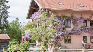 En toetages bygning med røde tegltagsten, en balkon og lilla blomstrende slyngplanter.