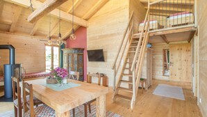A wooden cabin interior with a dining table, chairs, a ladder, a fireplace, and a television.