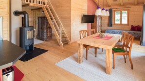 A cozy cabin interior with a wooden dining table, chairs, a fireplace, a TV, and a staircase.