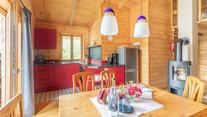 Interior de una cabaña de madera con cocina, comedor y estufa de leña.