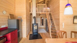 Interior de una cabaña de madera con cocina, comedor y una escalera que sube a un dormitorio tipo altillo.