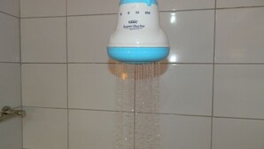 A bathroom with white tiled walls and a showerhead labeled "TAME SuperDucha".