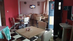 A dining area with checkered flooring, multiple tables and chairs, a television mounted on the wall, and a sink with a mirror.